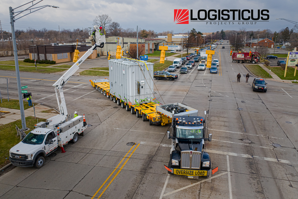 A large truck labeled OVERSIZE LOAD transports a massive white container on a yellow trailer through a city intersection, followed by police cars. A utility worker in a bucket truck works on overhead lines. The LogistiCus logo is visible.