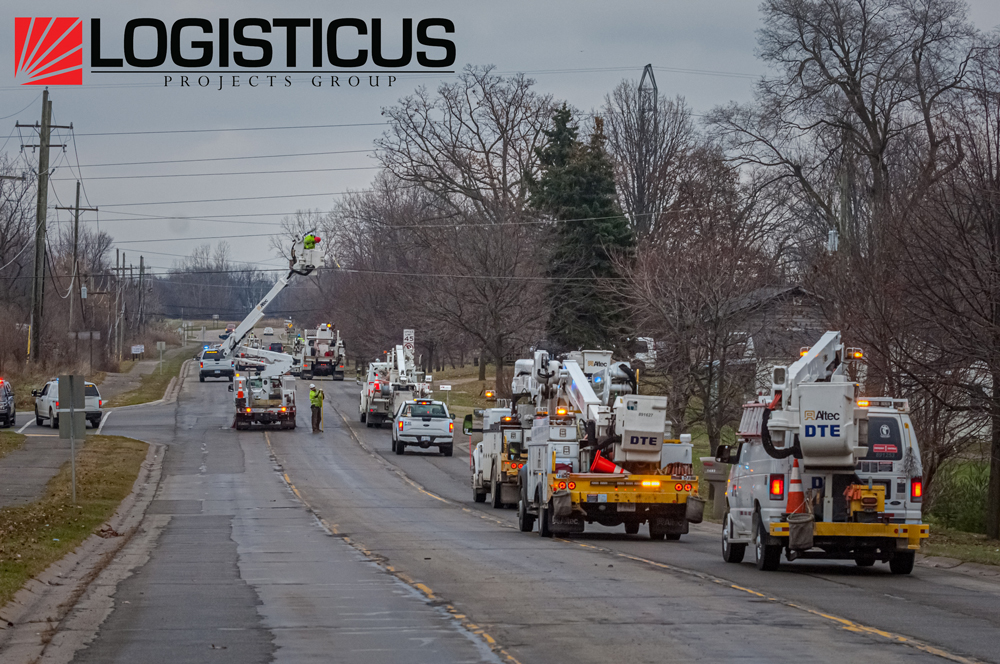 Utility trucks and crews from DTE Energy work on power lines along a suburban road lined with bare trees. Several vehicles are parked on the roadside under an overcast sky. LOGISTICUS PROJECTS GROUP logo appears at the top left.