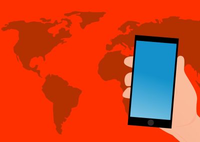 A hand holds a smartphone with a blue screen in front of a red background featuring a dark red world map.