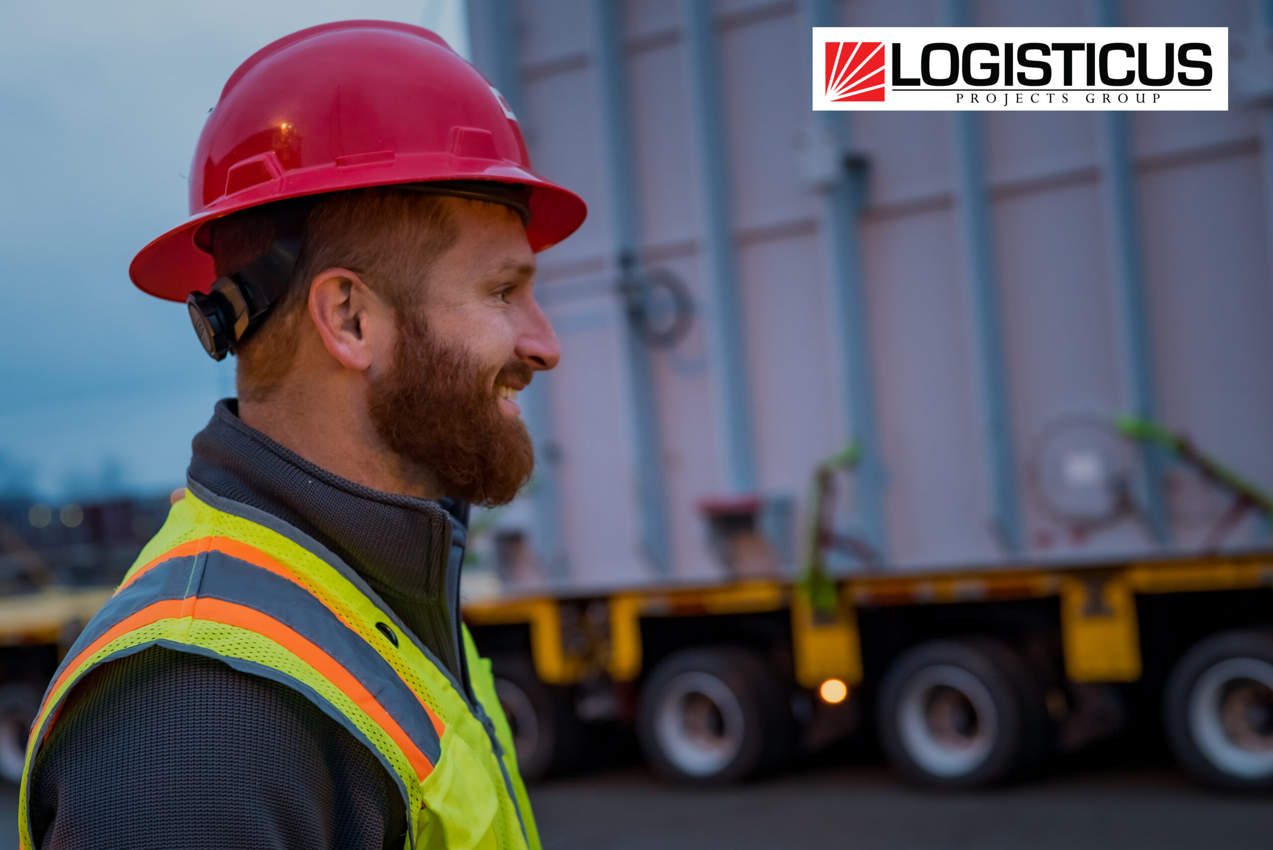 2-8 A bearded man in a red hard hat and safety vest smiles while standing outdoors near industrial equipment. The LOGISTICUS Projects Group logo appears in the top right corner.