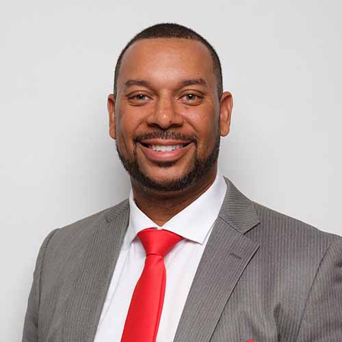 Jason Murchison wearing a gray suit, white shirt, and red tie smiles at the camera against a plain white background.